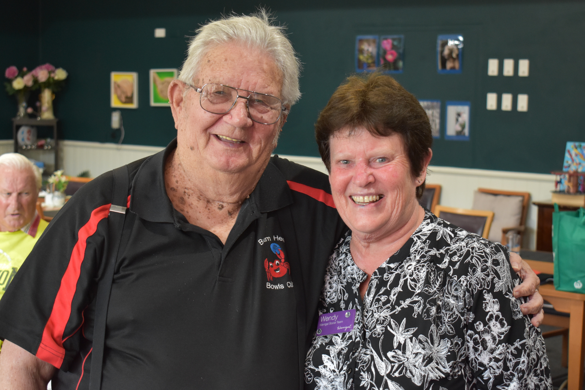 A warrigal social customer and staff member smile at the camera with their arms around each other in a friendly manner.