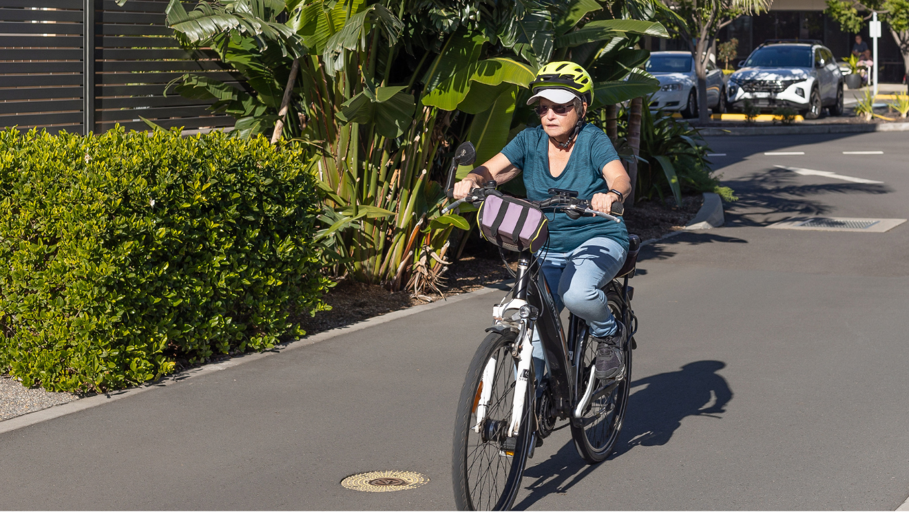 Warrigal Shell Cove village resident riding bike down path with green gardens beside it.