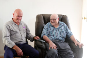 Male Warrigal staff member laughing with home services aged care customer as he sits in recliner.