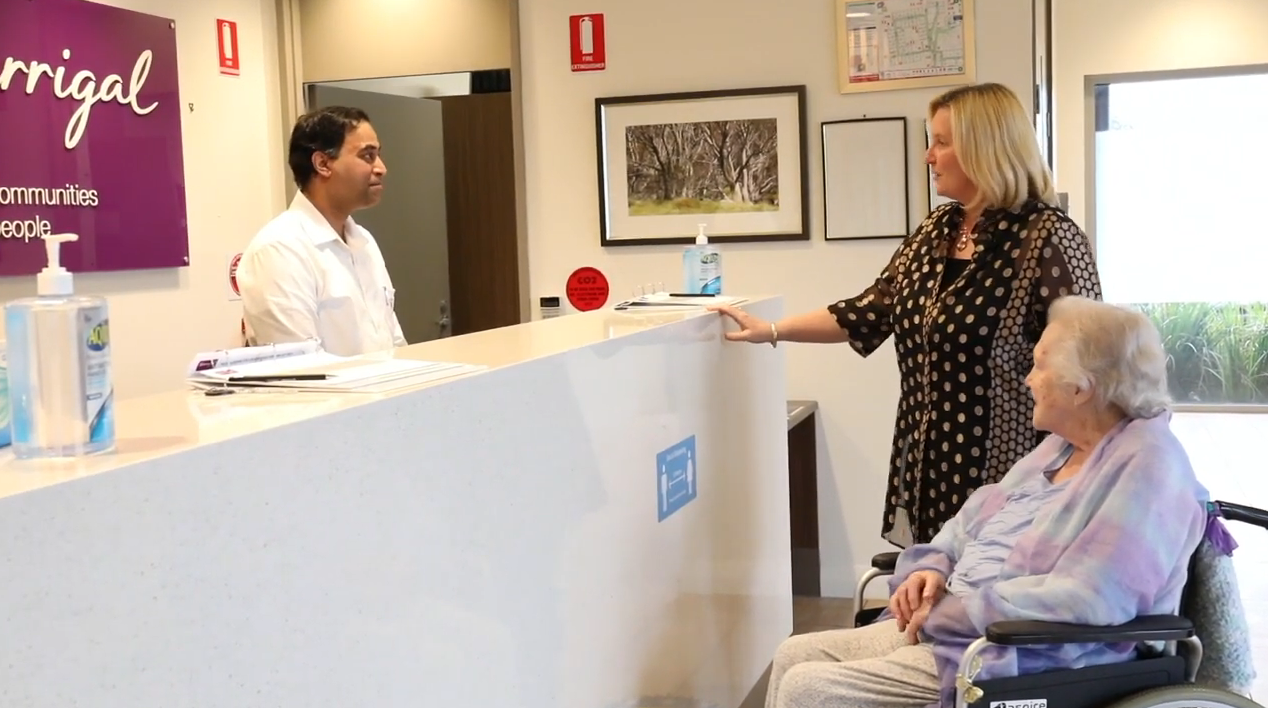 Warrigal video thumbnail showing a staff member smiling at a resident and their family member before a tour.