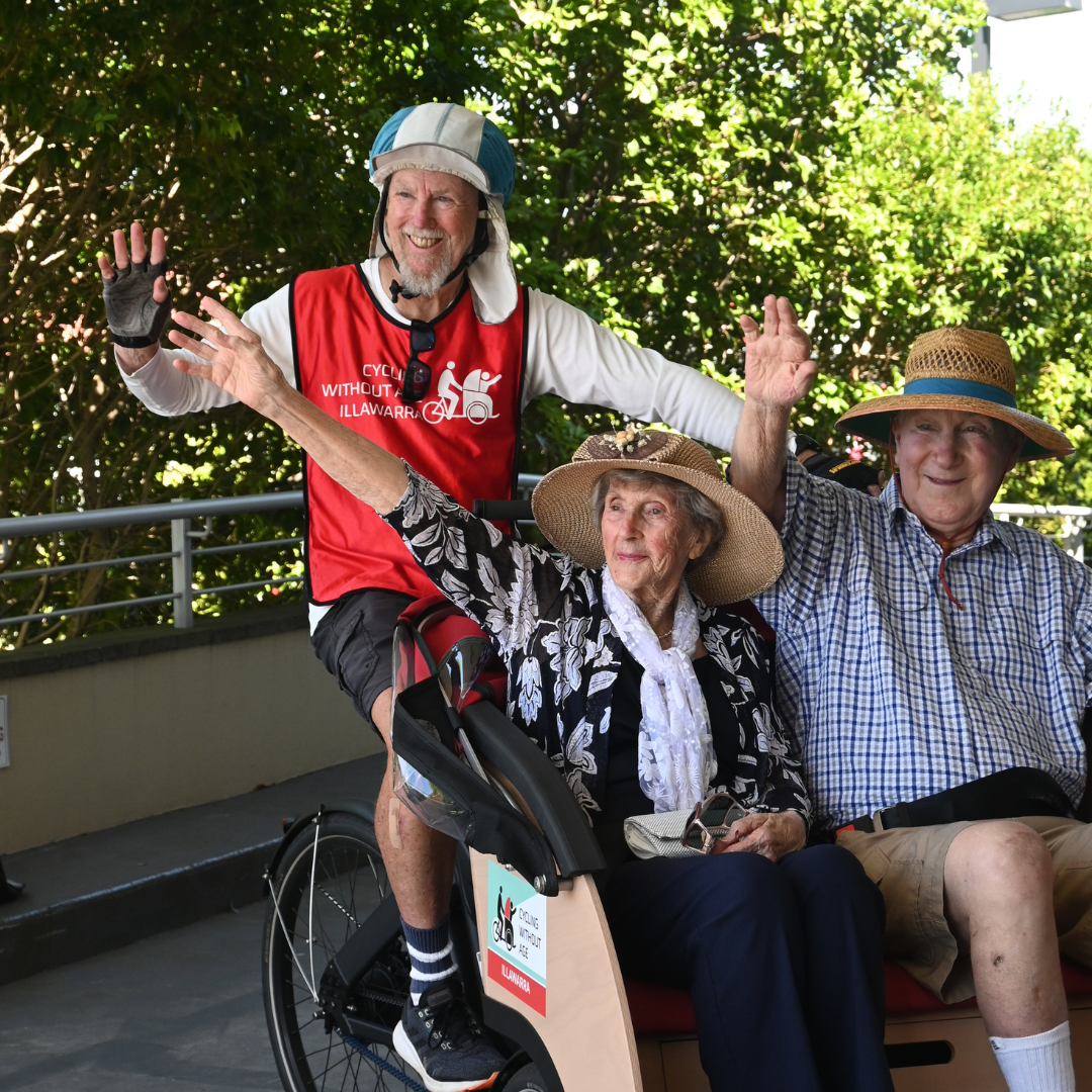 Waving smiling residents on board trishaw bike at Warrigal Wollongong