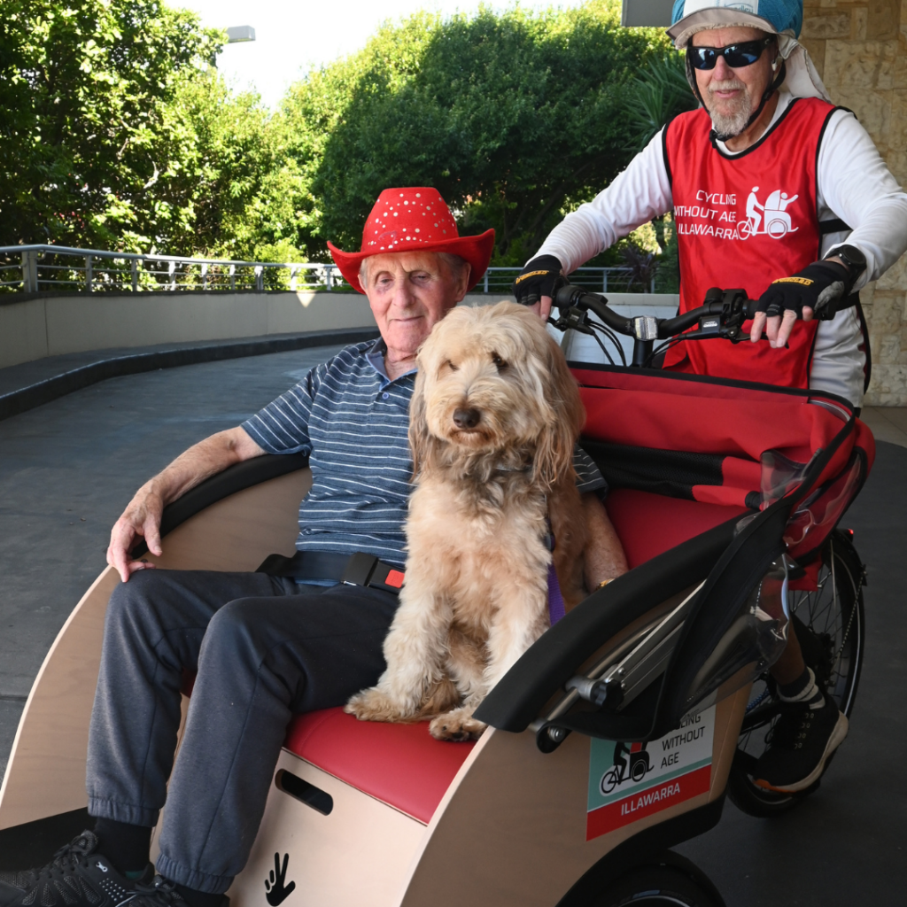 Smiling residents on board trishaw bike at Warrigal Wollongong with Benji the dog