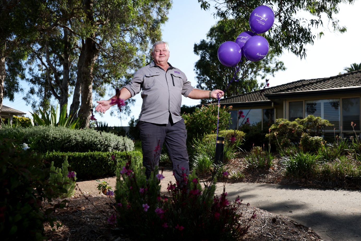 Warrigal staff member smiles at camera holding purple balloons with logo